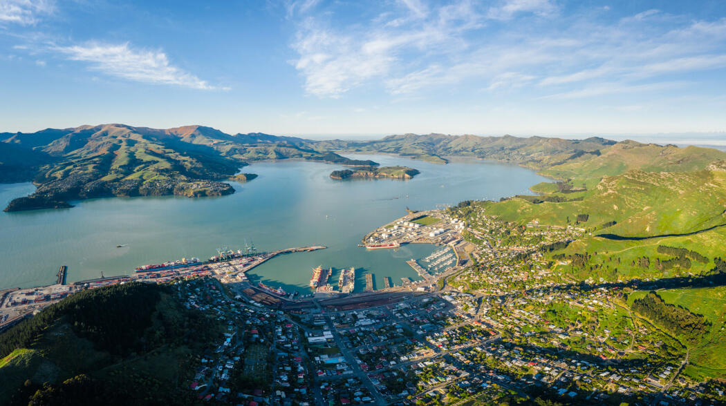 Aerial view of Lyttleton Harbour, a coastal harbour in New Zealand surrounded by hills, with a port, marina, and urban area along the shoreline.