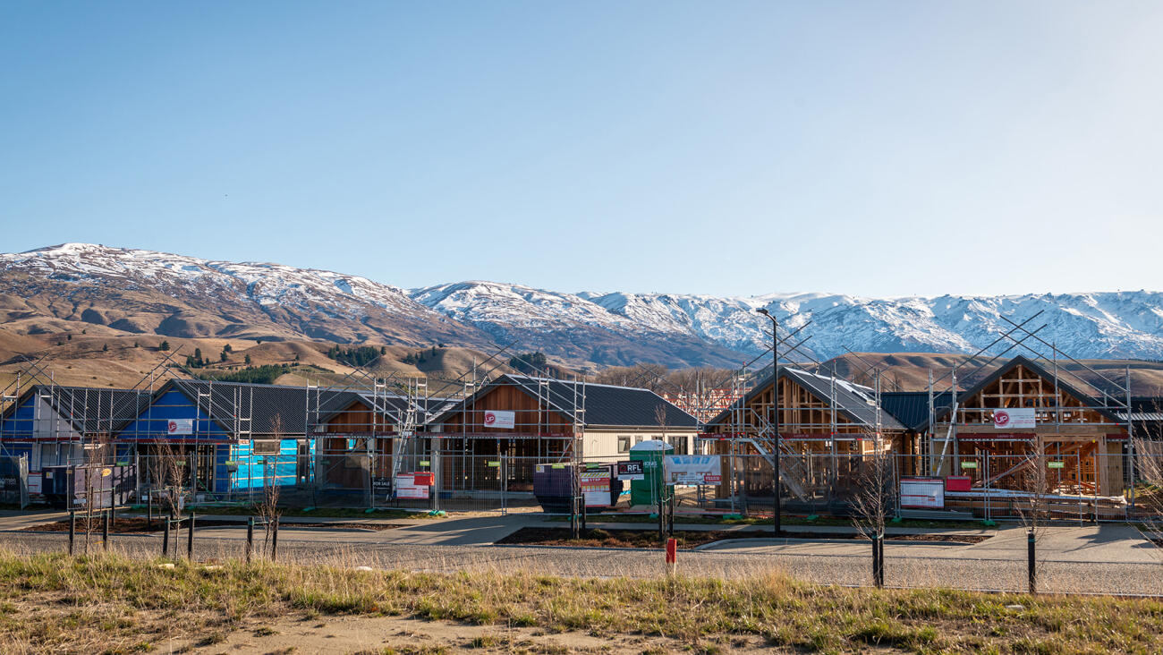 Residential houses under construction in a new subdivision, with snow-capped mountains in the background.